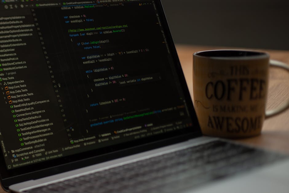 A close-up image of a laptop screen displaying lines of code, positioned on a wooden desk with a slight tilt showing the keyboard and part of the screen. To the right of the laptop, there is a ceramic